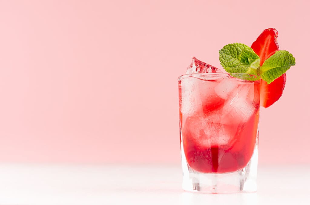 A pink background with a glass of muddled strawberries illustrates cocktail gardening